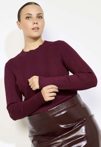 Bordo ribota dzija džemperis ar apaļu kakla izgriezumu un garām piedurknēm, kombinēts ar spīdīgu brūnu augsto jostasvietu svārku.