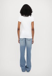 Camiseta blanca de manga corta combinada con unos pantalones vaqueros holgados de color azul claro. Los pantalones tienen una textura desteñida y dos bolsillos traseros, sin logotipos visibles.