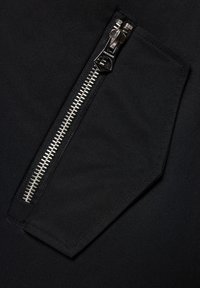 Czarna tkanina o fakturowanej powierzchni z zamykaną kieszenią, srebrnym metalowym zamkiem błyskawicznym i prostokątnym klapą. Akcenty w postaci kontrastowych szwów.