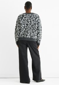 Strickpullover mit grauem Hintergrund und weißem Leopardenmuster. Tragen mit weit geschnittenen schwarzen Jeans und schwarzen Ballerinas.
