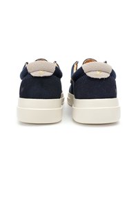 Zapatillas de ante azul marino con un acento en el talón beige, punta redondeada y suela de goma de color claro. Incluye acentos laterales funcionales.