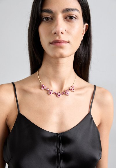 Auksinis kaklo papuošalas su purpuriniais akmenimis gėlių raštais, dėvimas virš juodos satino kamizolos. Paprasta grandinėlė su sudėtingais akcentais.