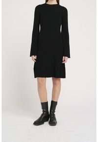 Svart ribbad klänning med långa ärmar, rund halsringning och utsvängd nederdel. Buren med svarta ankelstövlar. Slät textur.