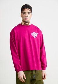 Koszula z długim rękawem w jasnym magencie z bawełny, z białym wzorem graficznym na lewej piersi oraz ściągaczami na rękawach.