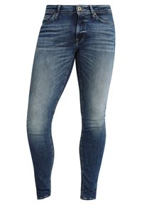 Vaqueros de denim azul de corte slim con cierre frontal de botón y cremallera, diseño de cinco bolsillos y detalles de lavado desgastado en los muslos y las rodillas.