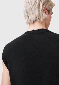 Melns piedurkņu trikotāžas tops ar fakturētu audumu, apaļu kakla izgriezumu un frēzētu apdari uz muguras apkakles.