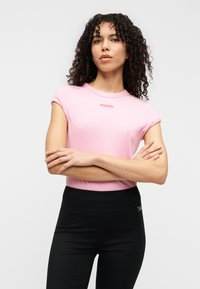 Ανοιχτό ροζ ριμπ κοντομάνικη μπλούζα με στρογγυλή λαιμόκοψη και ραμμένη λεπτομέρεια με λογότυπο· συνδυασμένη με μαύρο ψηλόμεσο κολάν.