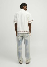 Hvid kortærmet skjorte med røde broderede detaljer ved kanten, parret med lyseblå slidte jeans og brune sko.