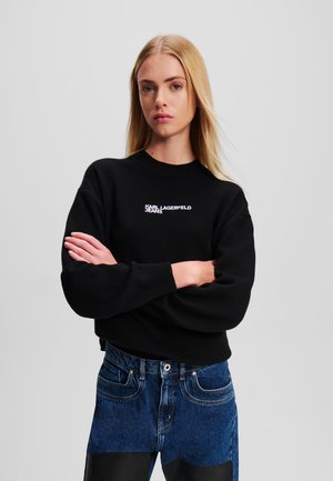 Felpa nera con colletto tondo e spalle scese, caratterizzata dal logo bianco "Karl Lagerfeld Jeans". Indossata con jeans in denim blu a vita alta.