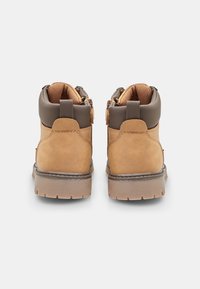 Stivaletti alla caviglia in suede marrone con colletto imbottito, chiusura con zip e suola in gomma. Presentano cuciture di contrasto e dettagli di durata.