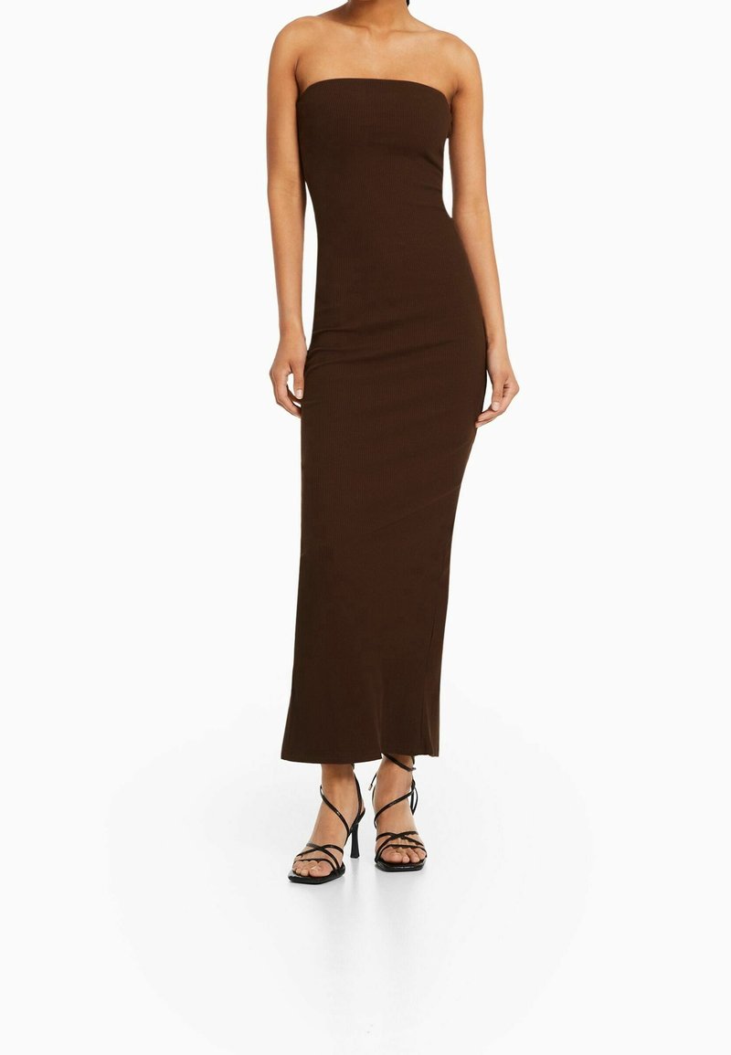 Robe maxi sans bretelles marron avec une silhouette ajustée et une texture côtelée, associée à des talons noirs à lanières, mettant en valeur un design ouvert au niveau des orteils.