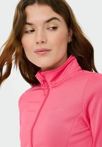 Giacca rosa con zip e collo alto, realizzata in tessuto liscio. Presenta un logo discreto, un design aderente e dettagli di cuciture visibili.