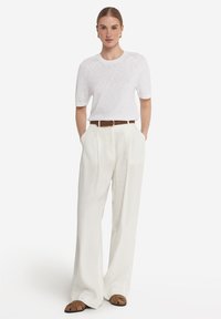 Vit linnet-shirt med kort ärm, kombinerad med högmidjade, vida off-white byxor och brunt läderbälte. Bruna slidesandaler.