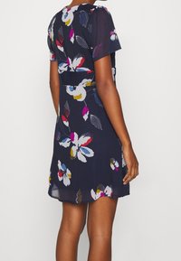 Kurzes, ärmelloses Kleid in Marineblau mit floralem Muster in Weiß, Pink, Gelb und Blau, tailliert in der Mitte und mit einem lockeren, fließenden Rock.