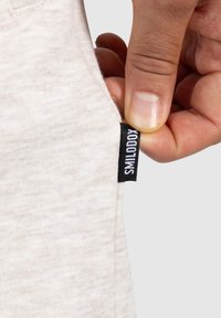 Tejido gris claro con una textura suave, siendo estirado para revelar una etiqueta negra con el texto "SMILODOX", visible en la costura.