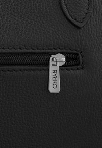 Sac en cuir noir avec une surface texturée, une fermeture éclair argentée portant une étiquette gravée "RYŁKO" et une couture discrète le long du bord.