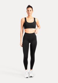Brassière de sport noire et leggings taille haute en tissu extensible. Détails remarquables : une poche latérale sur les leggings et un design épuré.