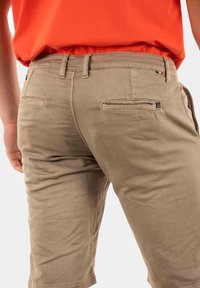 Pantaloni corti color khaki realizzati in un morbido tessuto misto cotone, con tasche posteriori munite di pattina e cuciture a vista, arricchiti da un sottile dettaglio del marchio.