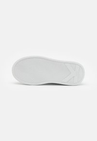 Suola di sneaker bianca con una texture ondulata e un pronunciato logo "K" vicino al tallone. Bordi arrotondati con una finitura liscia.