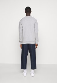 Grå sweatshirt med avslappnad passform, ribbade ärmslut och midja, tillsammans med vida mörk denimbyxor och vita sneakers.