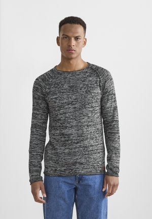 Szary i czarny melanżowy sweter z długimi rękawami, okrągłym dekoltem i ściągaczami, w połączeniu z niebieskimi dżinsami. Minimalistyczny design.