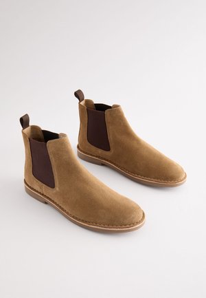 Beežid seemisnahast Chelsea saapad pruunide elastsete külgedega, haaramisriba ja lameda kummist tallaga. Omavad sileda tekstuuri ja ümarat varbakuju.