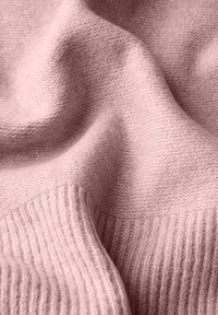 Tissu tricoté rose, présentant une texture lisse avec un bord côtelé. Le matériau semble doux et est légèrement drapé.