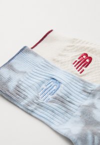 To par sokker: en kremfarget med rød logo, og en lyseblå med stripete tekstur og en liten blå logo, med ribbestrikkede mansjetter.