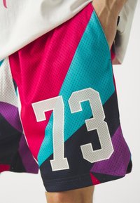 Pantalones cortos deportivos coloridos con un diseño geométrico en rosa, azul y negro, con el número blanco "73" impreso de manera prominente. Hechos de malla transpirable.
