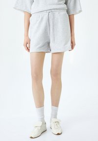 Grijze trainingsshorts met een elastische tailleband en trekkoord. Draagt witte sokken en bijpassende sneakers. Glad materiaal, casual ontwerp.
