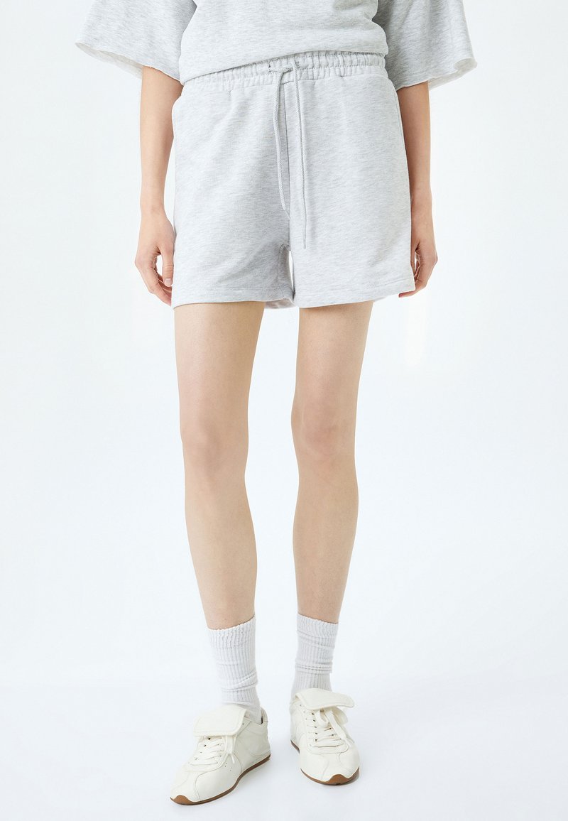 Grijze trainingsshorts met een elastische tailleband en trekkoord. Draagt witte sokken en bijpassende sneakers. Glad materiaal, casual ontwerp.