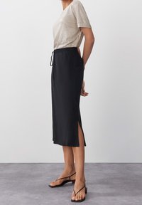 Mustapitu midi-hame, jossa on sivureiät, joustava vyötärö ja naru. Yhdistetty vaaleanväriseen lyhythihaiseen toppiin.