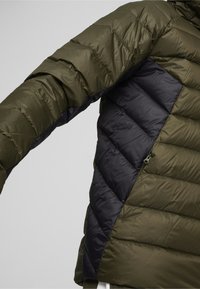 Polstret jakke med olivengrøn yderside og mørkeblå sidelæder i et diagonalt design. Struktureret finish og lynlåslomme detaljer.