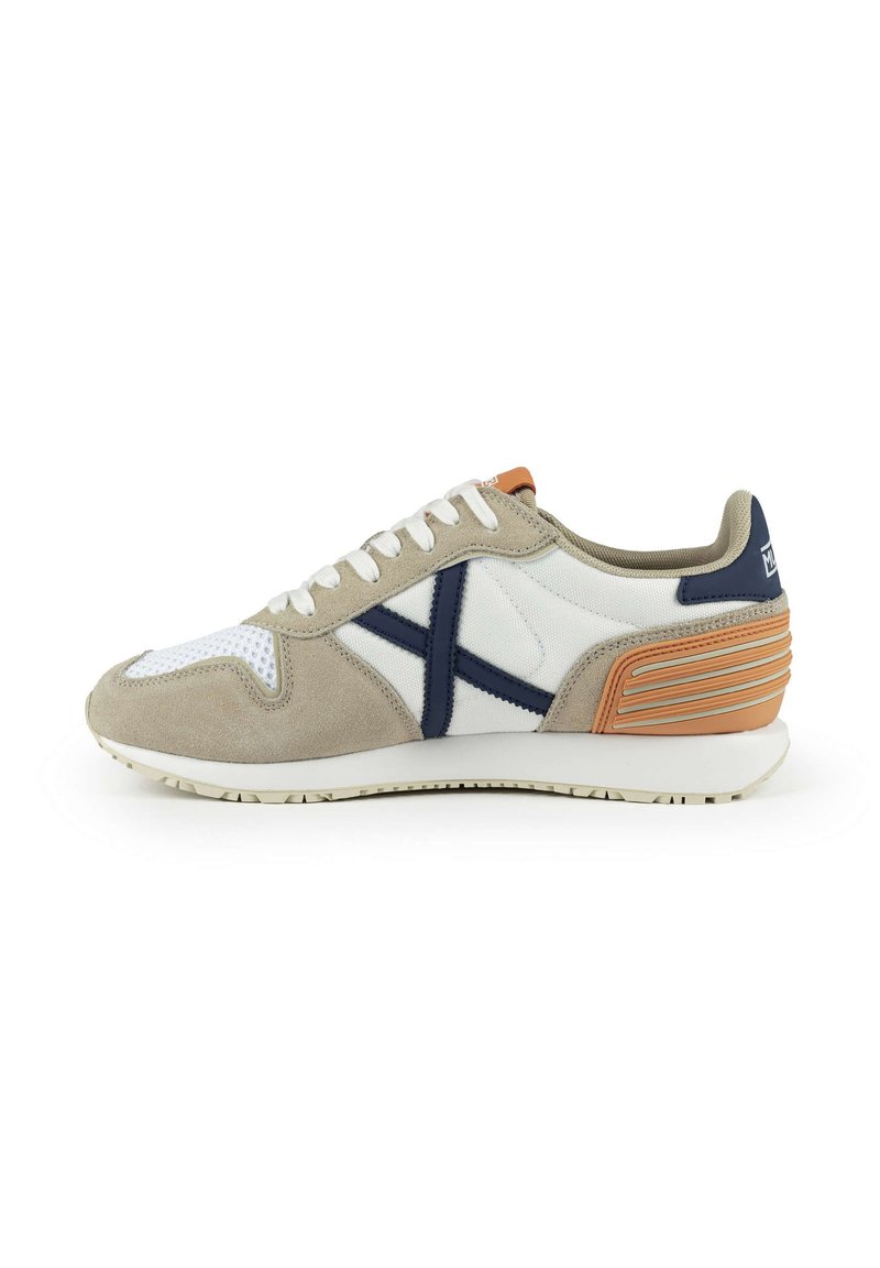Chaussure de sport en suède beige et en mesh blanc, avec des accents bleus, un design de talon texturé et une semelle en caoutchouc blanc avec des motifs de semelle.