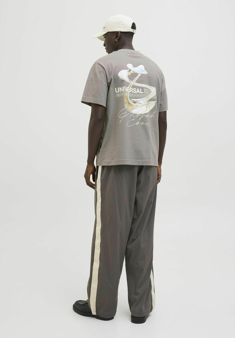 Pelēks pārmērīgs t-krekls ar grafisku apdruku aizmugurē, kopā ar pelēkiem sporta biksēm ar sānu svītrām un melnām kurpēm. Beisbola cepure iekļauta.