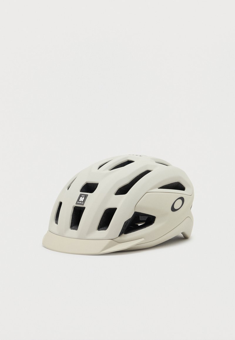 Casco de bicicleta beige de tamaño mediano con múltiples ranuras de ventilación y una pequeña visera, con un logo negro de Oakley en el lateral.