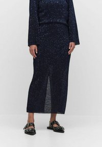 Navy blue neulepuku, joka koostuu kahdesta osasta ja siinä on teksturoitu kuvio. Paidassa on pitkät hihat ja hameessa on sivuaukko. Mustat litteät sandaalit, joissa on soljet.