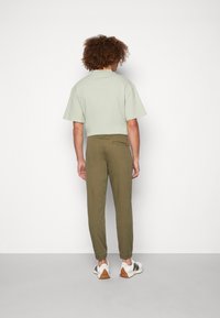 Camiseta de manga corta verde claro combinada con pantalones ajustados verde oliva y zapatillas blancas con detalles en gris y marrón.