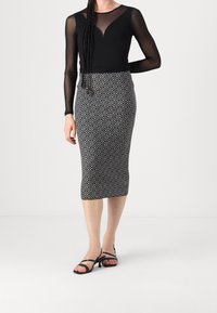 Haut en maille noire à manches longues avec un décolleté en V et une jupe crayon à motifs noir et blanc. Les sandales ont des lanières fines et un petit talon.