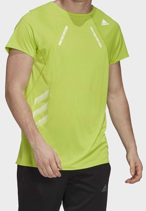 Mężczyzna w neonowo zielonym, krótkim rękawie koszulce do biegania Adidas i czarnych spodniach Adidas, stojący na białym tle.