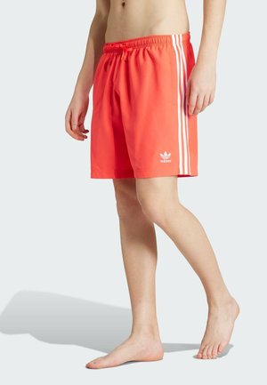 Lys korallfärgade badshorts i lätt tyg, med elastisk midja, dekorativ dragsko och tre vita vertikala ränder på sidorna.