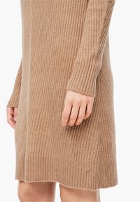 Ribbed pletené šaty ve světle hnědé barvě, s dlouhými rukávy a mírně rozšířeným lemem. Měkká textura s viditelným šitým detailem.