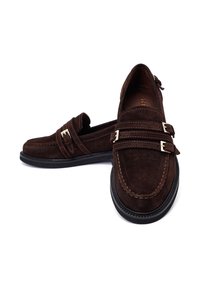 Mocassini in suede marrone con accenti a doppia fibbia, dettagli cuciti e suola in gomma. Presentano un design slip-on e punta arrotondata.