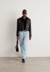 Svart lær cropped bikerjakke, svart skjorte, lys blå høyt liv jeans, svart håndveske og mørke ankelstøvler. Glatte teksturer og tettsittende design.