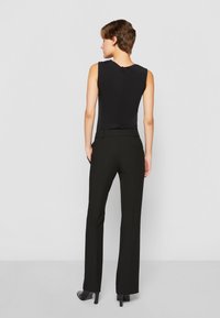 Top nero senza maniche con una texture liscia, abbinato a pantaloni neri su misura. Slim-fit, con dettagli sulla tasca posteriore.