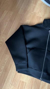 Sudadera negra con cremallera, de textura suave, con un bolsillo delantero y costuras reforzadas en los puños y el dobladillo.