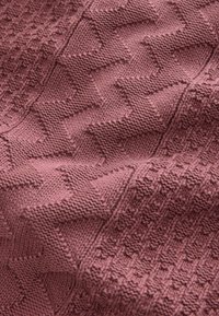 Tissu tricoté rose avec des motifs en zigzag en relief et des motifs géométriques texturés créant un effet tridimensionnel.