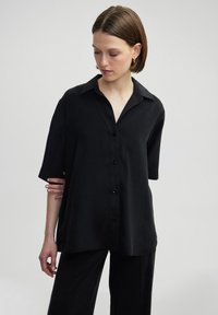 Black short-sleeve shirt with a button-up front, a classic collar, and a loose fit. Smooth texture, paired with matching black pants.