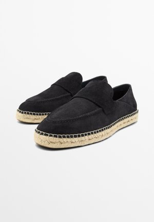 Sorte loafers i ruskind med beige jute-såler i espadrille-stil vist på en hvid baggrund, vinklet for at vise deres profil og overdel.