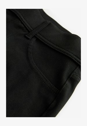 Black denim fabric with a textured surface, featuring a front pocket, belt loops, and stitched detailing along the edges.
